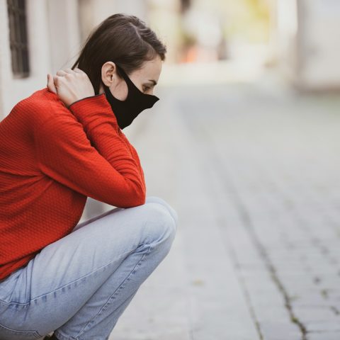 woman in red sweater and blue denim jeans sitting on concrete pavement