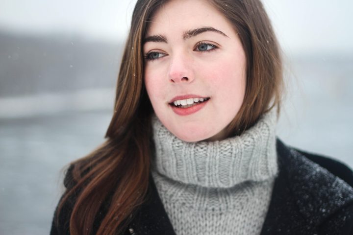 Vrouw in oversized wollen jas met gelaagde knitwear, silhouet zichtbaar door riem op taille